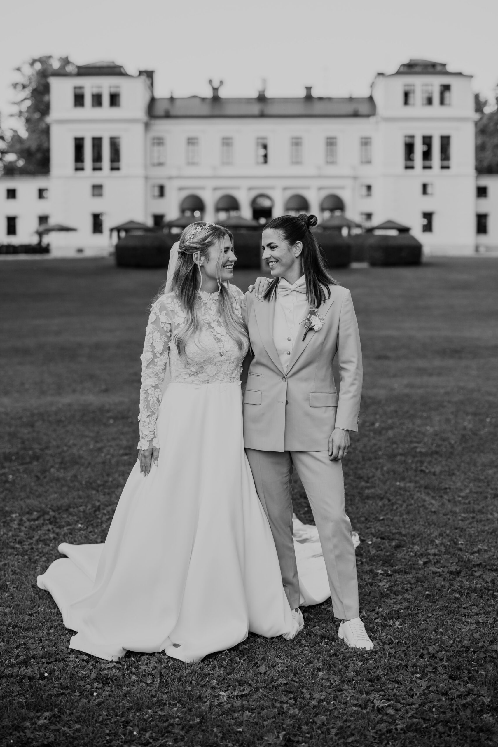 brudpar står tillsammans i bröllopskläder framför rånäs slott på gräsmattan